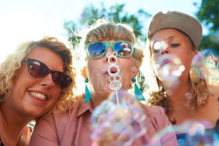 Photo for Women, friends and bubbles for blowing outdoor with sunglasses on weekend, break or holiday for relax and summer. People, happy and plastic wand or toy for playing or leisure on vacation or adventure. - Royalty Free Image