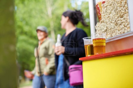 Photo for Beer, popcorn and vendor at festival closeup outdoor with people on blurred background for event or party. Summer, food or snack with alcohol in plastic cup on counter for drinking and celebration. - Royalty Free Image