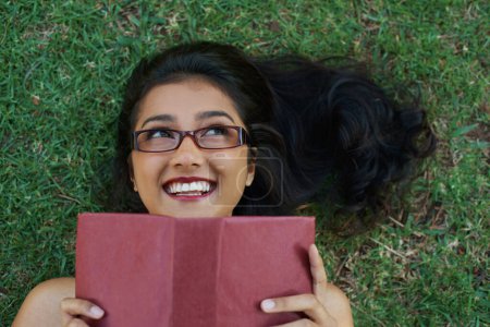 Photo for Woman, happy and reading book on grass, literature and smiling for fiction or fantasy story. Female person, nature and relaxing on lawn for knowledge, textbook and student studying in garden outdoors. - Royalty Free Image