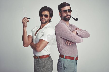 Photo for Fashion, men and sunglasses or pipe in studio with vintage model, hipster outfit and confidence with arms crossed. Friends, people and attitude with 70s style or retro clothes with white background. - Royalty Free Image