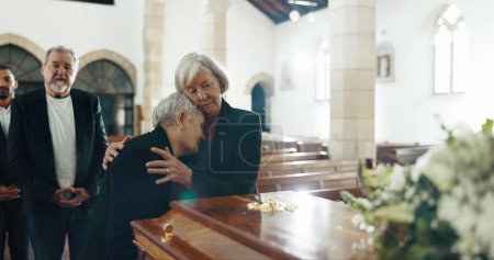 Photo for Senior women, hug and funeral in church for comfort, support and care with crying, sad and religion. Family, friends and embrace for death, loss and console with love, empathy and faith by coffin. - Royalty Free Image
