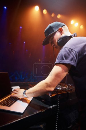 DJ, man and laptop at nightclub for concert with spotlights, turntables and live music show. Professional person with crowd, playlists and mixing deck for party, rave or festival in Portugal.