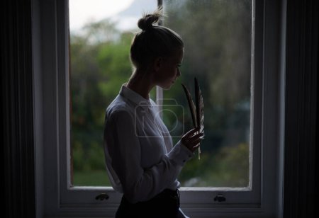 Photo for Woman, feather and window in home for writing in dark room and mysterious aesthetic for artistic pose. Female writer, dim light and ink pen with thinking, author and old school setting for creativity. - Royalty Free Image