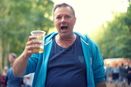 Téléchargez les photos : Mature, homme et portrait avec bière en plein air au festival dans le parc, bois ou fête dans la nature. Personne, boire et trinquer avec une tasse en plastique avec de l'alcool pour la célébration lors d'un événement en forêt ou en été. - en image libre de droit