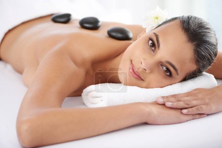 Photo for Smile, hot stone and portrait of woman with massage at spa for wellness, health and back treatment. Self care, cosmetic and young female person relaxing for warm rock therapy at natural beauty salon - Royalty Free Image