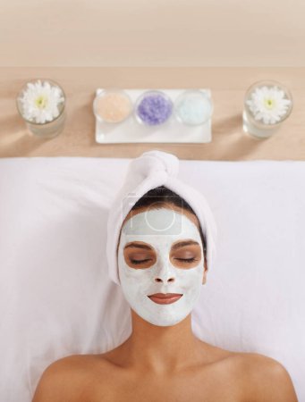 Photo for Woman, face mask and cosmetology for beauty in spa, detox and cosmetic treatment for salon facial. Person, relax and aromatherapy with natural clay on skin, calm and skincare for dermatology on bed. - Royalty Free Image