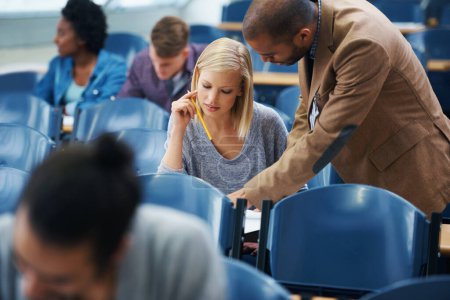 Photo for University, helping and professor with student in classroom studying for test, exam or assignment. Education, learning and teacher talking and explaining college information to woman in lecture hall - Royalty Free Image