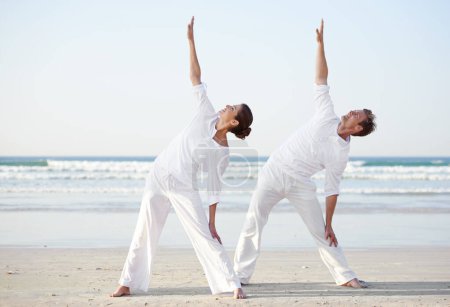 Téléchargez les photos : Couple, yoga et pose, fitness sur la plage pour zen et bien-être, voyage et pleine conscience avec guérison holistique. Personnes en plein air, l'exercice et l'équilibre, l'entraînement ensemble pour coller avec la mer et la nature. - en image libre de droit