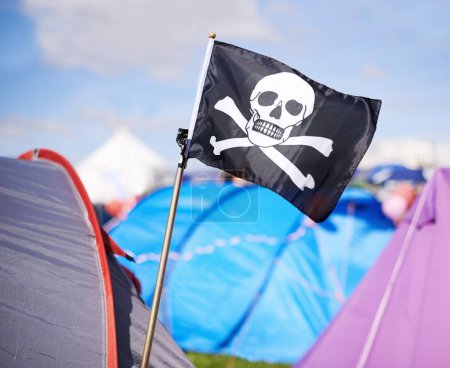 Photo for Pirate flag, tent and camping at festival outdoor in summer for party, event or celebration closeup. Skull, crossbones or jolly roger in nature for performance, entertainment or adventure with crowd. - Royalty Free Image