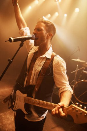 Photo for Night, singer and guitar with man on stage for music, performance and rock show. Event, spotlight and concert with male musician playing instrument at festival club for rave, disco and celebration. - Royalty Free Image