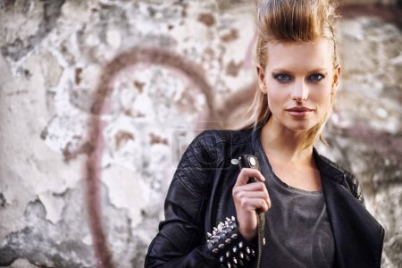 Photo for Woman, portrait and confident in edgy fashion with punk rock hairstyle, biker and cool in funky clothes by graffiti wall. Young model, face and leather jacket in urban town with trendy by street art. - Royalty Free Image