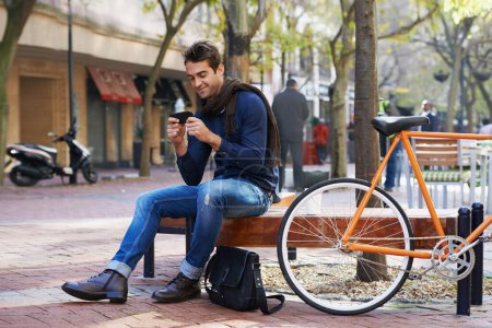 Photo for Phone, bike and business man in city, sitting on bench for break with social media browsing or app. Smile, contact and bicycle with confident young employee typing text message outdoor in urban town. - Royalty Free Image