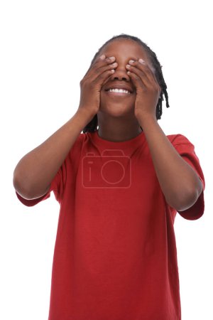 Téléchargez les photos : Enfant, garçon et couvrir les yeux avec les mains pour le secret ou la surprise, se cacher ou de protection, t-shirt rouge et sourire sur fond blanc. Emoji, heureux enfant africain ne cherche pas d'annonce ou de nouvelles en studio. - en image libre de droit