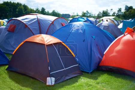 Téléchargez les photos : Tentes de groupe, colorées et camping dans la nature à l'extérieur d'un camping festival de musique. Rangée de verrières placées sur le sol lors d'un concert musical, d'un événement de divertissement et d'une célébration du carnaval en plein air sur herbe. - en image libre de droit