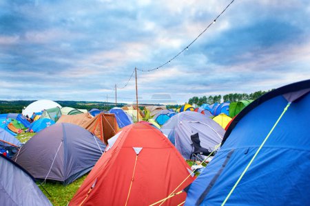 Téléchargez les photos : Camping, tentes et festival de musique en plein air dans le parc en vacances ou en vacances en été. Installation d'un camp, d'un site et d'un abri lors d'une fête, d'un événement ou d'un voyage à la campagne pour un concert, une aventure et un carnaval bondé. - en image libre de droit