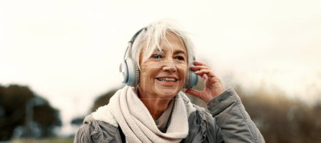 Photo for Old woman, headphones and listening to music outdoor, walking and wellness with audio streaming and energy. Podcast, radio and sound with female person on city bridge, exercise and travel with tech. - Royalty Free Image