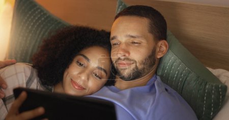 Téléchargez les photos : Couple, sourire et se détendre dans la chambre avec tablette le soir, film en streaming ou film. Heureux, la technologie et l'homme et la femme au lit sur les médias sociaux, navigation app en ligne et regarder la vidéo ensemble à la maison. - en image libre de droit