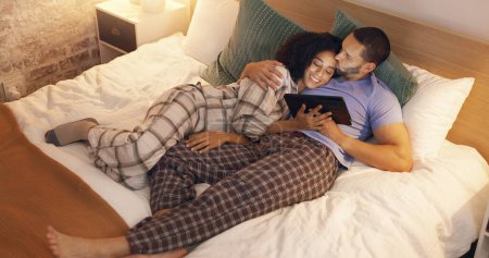 Téléchargez les photos : Couple, heureux et câlin dans la chambre avec tablette la nuit, film en continu et se détendre. Sourire, la technologie et l'homme et la femme au lit sur l'application de médias sociaux, regarder des vidéos en ligne et coller ensemble à la maison - en image libre de droit