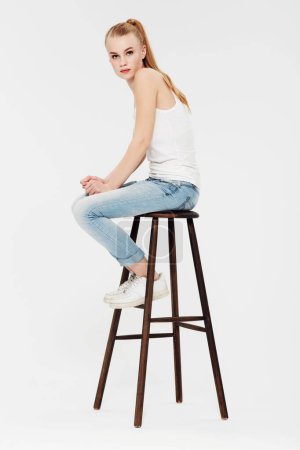Photo for Teenager, fashion and portrait on chair in studio and white background with confidence and pride. Beauty, face and girl with a ponytail in casual trendy style, jeans and relax in mock up space. - Royalty Free Image