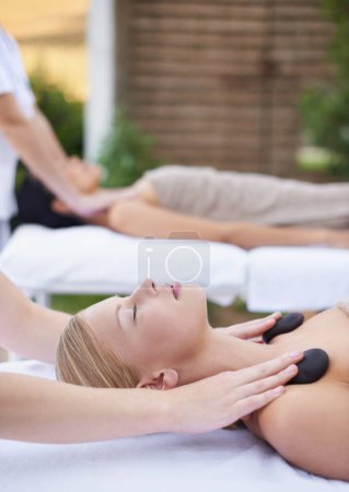 Photo for Women, health and massage with hot stones, wellness and peace with hands for shoulder at spa. People, comfort and zen for physical therapy by masseuse, body treatment and detox on bed at resort. - Royalty Free Image