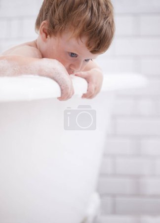 Photo for Baby, bath and clean with bubbles and curious in the bathroom at home for hygiene. Grooming, fresh and boy child cleaning for bodycare in the house while thinking for development and adorable growth. - Royalty Free Image