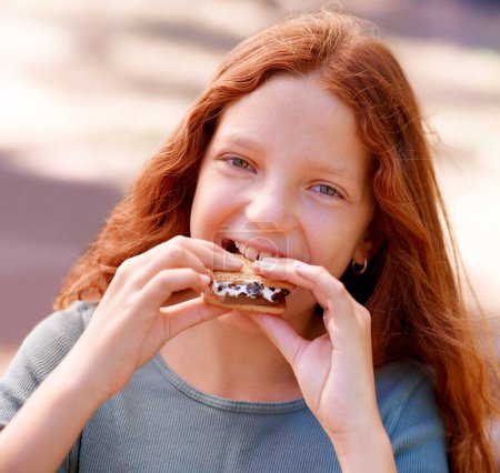 Photo for Child, eating and portrait with smores outdoor, camping and relax at barbecue with dessert or cookie. Happy, girl and hungry for biscuit with marshmallow in woods or forest on holiday or vacation. - Royalty Free Image
