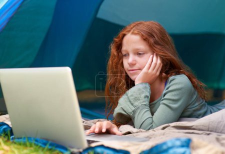 Photo for Child, girl and reading with laptop in tent for camping, social media and online movie with smile in nature. Person, face and kid with vacation outdoor on grass with gaming, relax and holiday fun. - Royalty Free Image