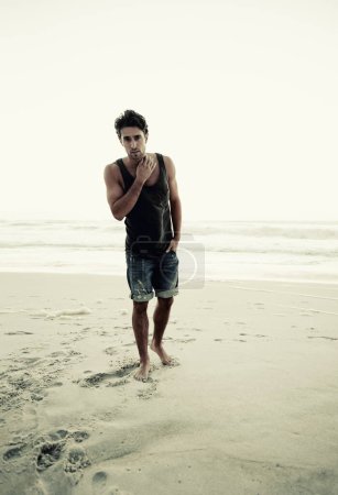 Photo for Man, beach and portrait at sunrise on holiday in trendy clothes, style and confident by waves. Person, ocean and sea on vacation, outdoor and tropical island in nature, footsteps and sand in Italy. - Royalty Free Image