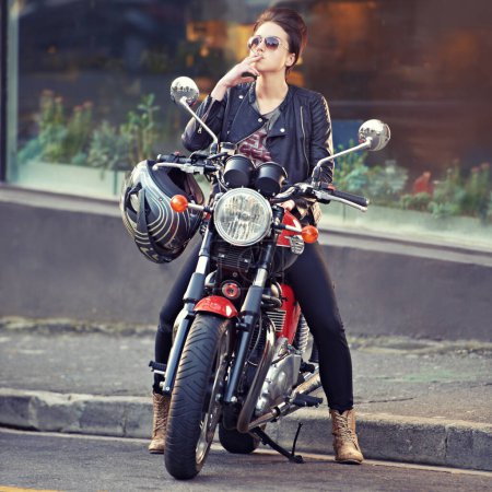 Photo for Motorcycle, leather and smoke with woman in city for travel, transport or road trip as rebel. Fashion, cigarette and sunglasses with model on classic or vintage bike for transportation or journey. - Royalty Free Image