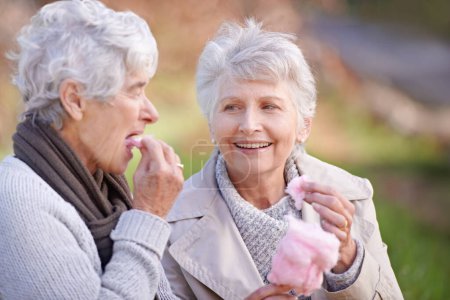 Photo for Senior women, eating and snack in nature with candy floss, together and relax on retirement outdoor. Elderly friends, happy and junk food on vacation in countryside, bonding and social in park. - Royalty Free Image