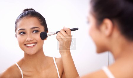Téléchargez les photos : Femme heureuse, brosse de maquillage et visage dans le miroir pour les cosmétiques, le toilettage ou la beauté dans la salle de bain à la maison. Femme sourire et appliquer fond de teint, rougir ou contour pour le traitement du visage en réflexion. - en image libre de droit