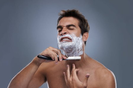 Photo for Man, shaving and razor with stress in studio for grooming, skincare and wellness with pain by grey background. Person, model and annoyed with beard, facial hair removal and cream for cosmetic change. - Royalty Free Image