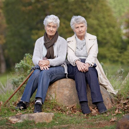 Photo for Senior friends, portrait or outdoor in nature on rock, together or bonding on retirement on holiday. Elderly women, serious or face on trip in countryside, winter or care for person with disability. - Royalty Free Image