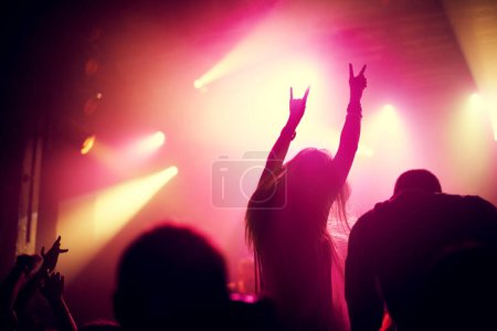 Photo for Rock, concert and people dance at night, event or party at music festival with fans in audience at stage. Crowd, energy and woman with hands in sign for metal, sound or social celebration at rave. - Royalty Free Image