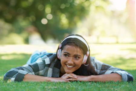 Photo for Woman, headphones and streaming music on grass, radio and internet for podcast in outdoors. Female person, happy and relaxing on lawn, weekend playlist and subscription for audio or sound on vacation. - Royalty Free Image