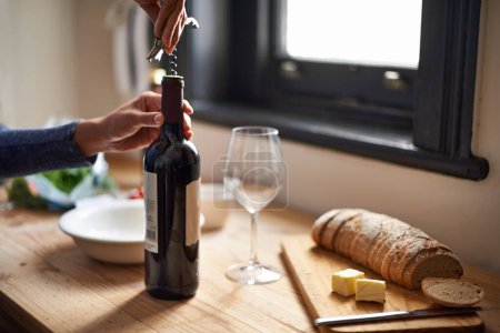 Photo for Hands, opening wine bottle and dinner on table, evening meal with corkscrew and glass, person preparing to drink for enjoyment. Alcoholic beverage, tools with cooking for dining and bread in kitchen. - Royalty Free Image