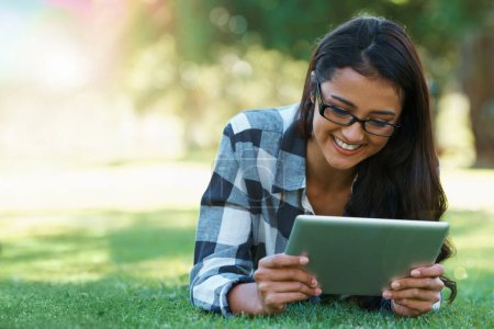 Photo for College, woman and reading on tablet in park with research, project or learning outdoor on campus. University, student and girl streaming online with ebook, education and studying on grass in garden. - Royalty Free Image