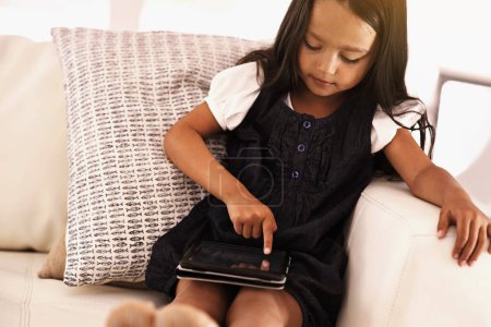 Photo for Kid, little girl and tablet on sofa for entertainment, movie or online streaming at home. Young female person or child browsing, scrolling or reading ebook with technology in living room at house. - Royalty Free Image