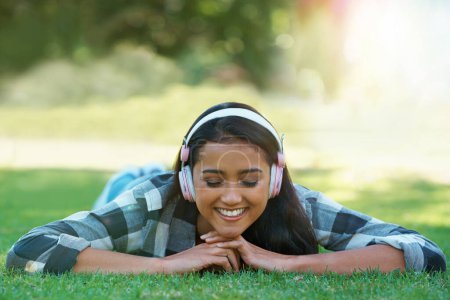 Photo for Woman, headphones and streaming song on grass, peace and calming podcast in outdoors. Female person, happy and relaxing on lawn, weekend playlist and subscription for audio or sound on vacation. - Royalty Free Image