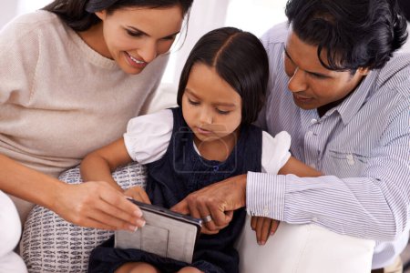 Photo for Happy family, tablet and reading ebook on living room sofa for social media, games or entertainment at home. Mother, father and daughter on technology for online streaming, relax or app at house. - Royalty Free Image