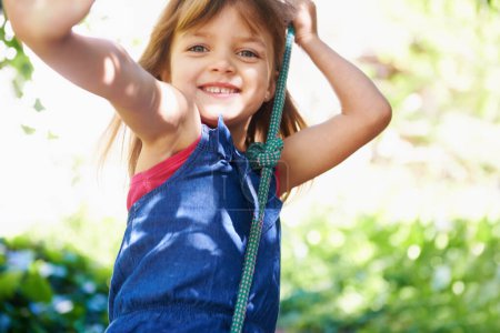 Téléchargez les photos : Portrait, sourire et enfant sur balançoire au parc, jouer au jeu et s'amuser en plein air dans la nature en été. Visage, enfant et fille sur la corde au jardin pour les loisirs, les loisirs et la promenade à l'aire de jeux en Australie. - en image libre de droit