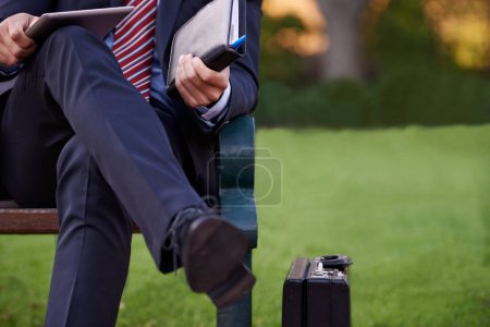 Closeup, tablet and business man on bench, park and planning with lunch break and professional. Employee, outdoor and consultant with suitcase and technology for ideas and shoes with fashion or relax.