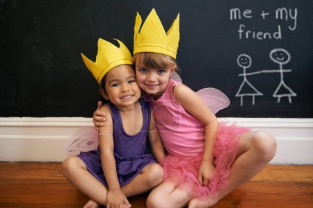 Photo for Little girls, friends and portrait with embrace, crown and smile for love and happiness. Children, youth and hug for face, fun and bonding with blackboard and fairy princess costume for dress up. - Royalty Free Image