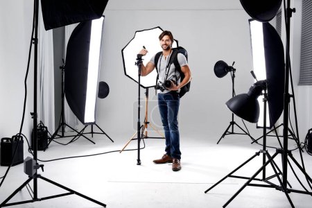 Photo for Photographer, portrait and lighting with equipment in studio for career, behind the scenes or electronics. Photography, person or happy with cameras, flash and shooting gear for photoshoot or passion. - Royalty Free Image