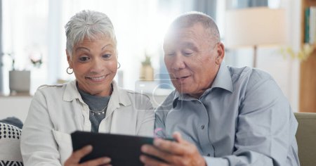 Photo for Senior, couple and tablet on sofa for online streaming, reading ebook or planning for retirement at home. Elderly people with digital technology for internet, happy with online choice and discussion. - Royalty Free Image