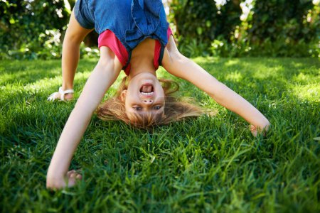 Photo for Child, back and bend or bridge or outdoor play in summer or flexibility game or practice, fun or backyard. Kid, face and excited or gymnastics stretching on grass lawn in London park, happy or garden. - Royalty Free Image