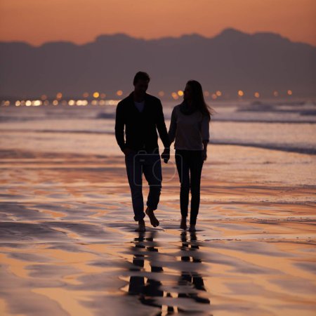 Photo for Silhouette, sunset and couple holding hands outdoor with back view and nature, travel and bonding for love and commitment. People walk on beach, trust and loyalty with adventure together and shadow. - Royalty Free Image