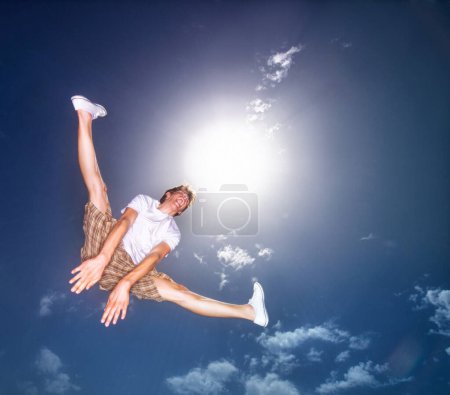 Photo for Boy, blue sky and jump outdoor with low angle, energy and lens flare of sunshine. Young teenager, below and leap in air by clouds in summer, moving and kid screaming for freedom with agile action. - Royalty Free Image