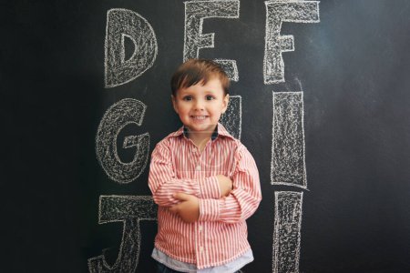 Photo for Child, boy and portrait with smile by blackboard with letters, alphabet or drawing in classroom at school. Kid, student and happy for knowledge, learning and chalkboard with illustration or preschool. - Royalty Free Image