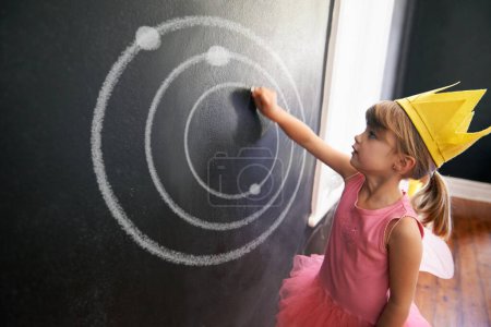 Photo for Child, board and drawing solar system for education with chalk in classroom with costume for creative, learning and guidance. Kid, chalkboard and crown for picture student in school for knowledge. - Royalty Free Image